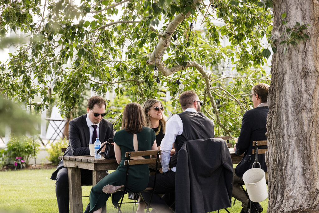 Group of people in business attire having an outdoor meeting at a wooden table under a tree.