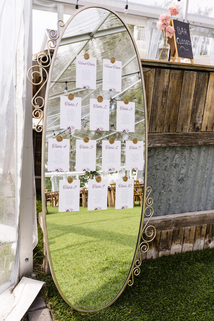 An ornate mirror displaying a wedding seating arrangement next to a rustic wooden bar with a "bar closed" sign.