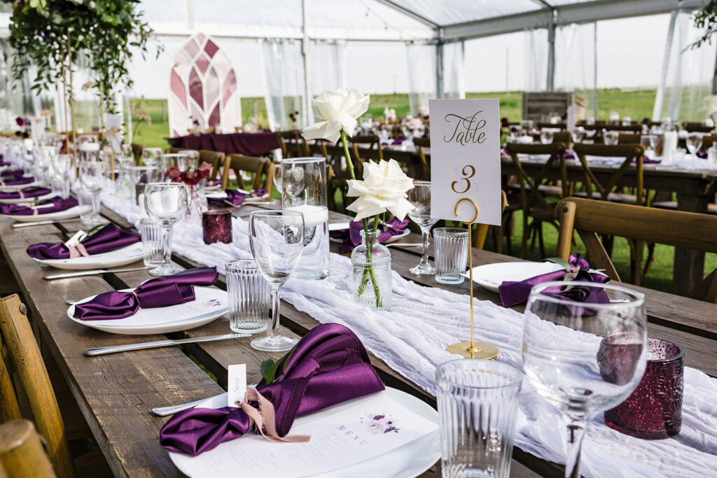 Elegant wedding reception table setting with a purple and white color theme inside a tent. A Garden Wedding with Pops of Plum