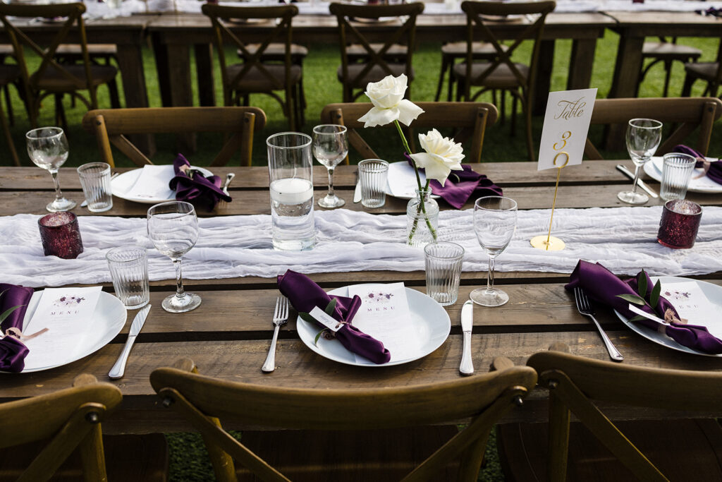 Elegant outdoor wedding table setting with purple napkins and white floral centerpieces. A Garden Wedding with Pops of Plum