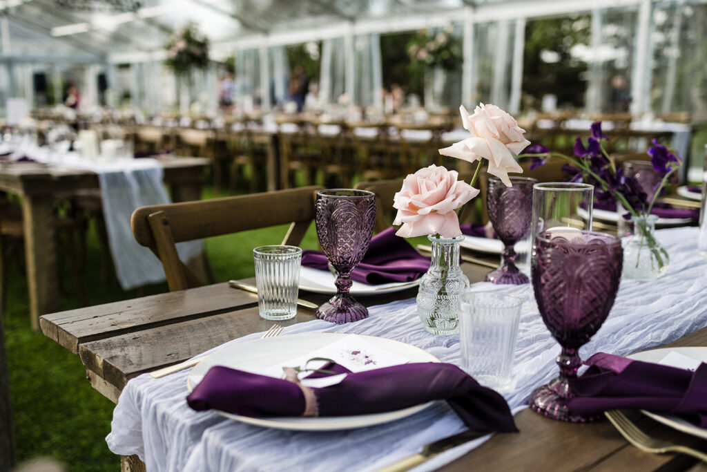 Elegant dining setup for an event with purple accents and floral decorations. A Garden Wedding with Pops of Plum