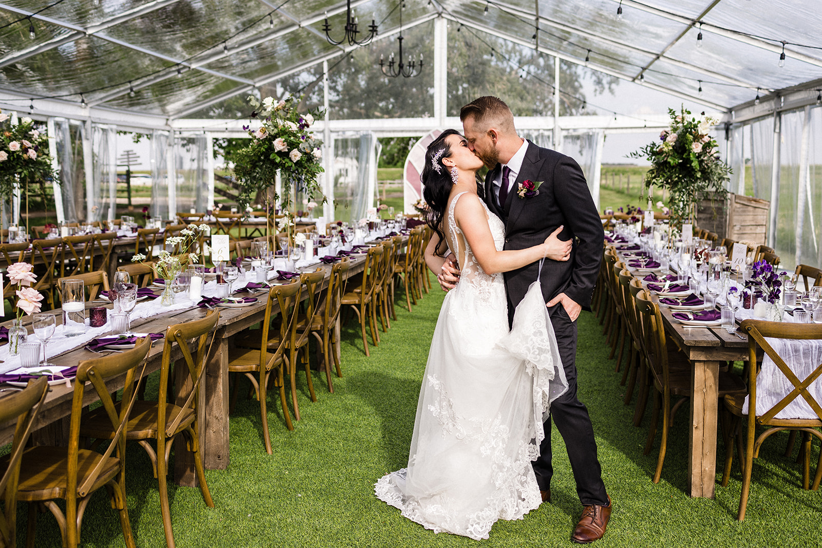 Bride and groom sharing a kiss inside a glasshouse wedding venue decorated with flowers and set tables.