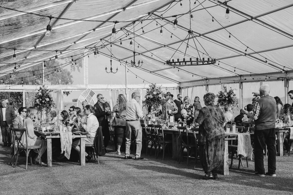 Guests mingling and dining at an outdoor event under a tent.