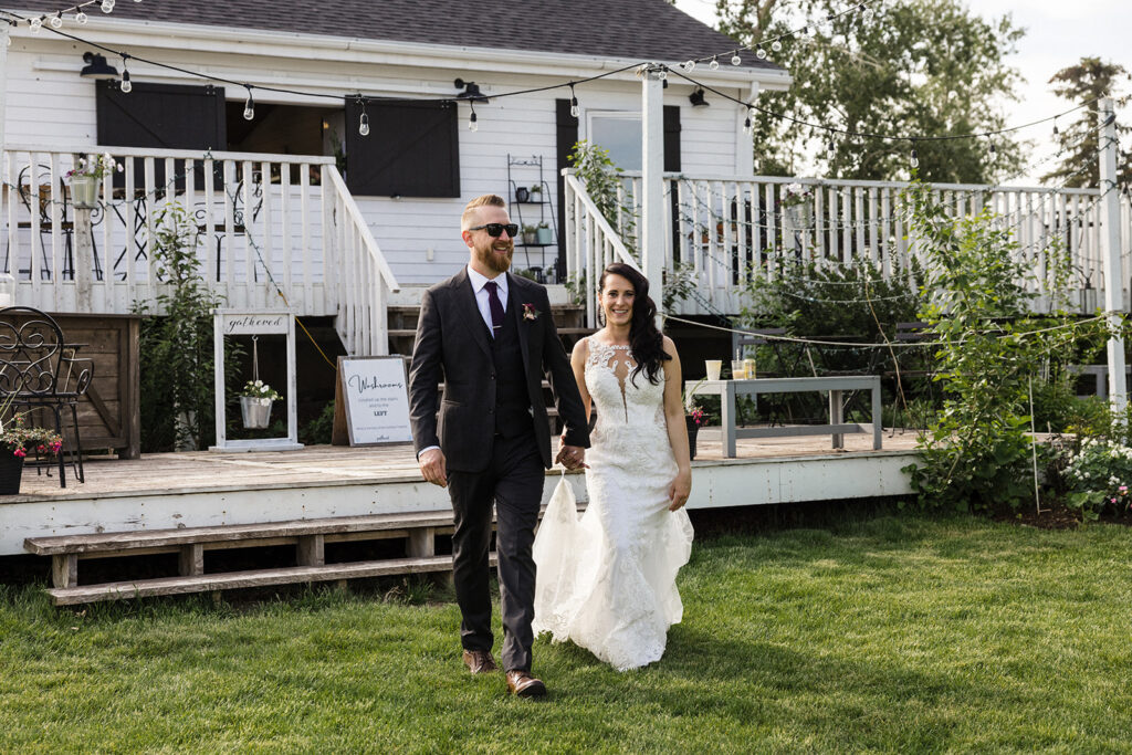A bride and groom walking hand in hand with smiles, in front of a house with a decorated porch.