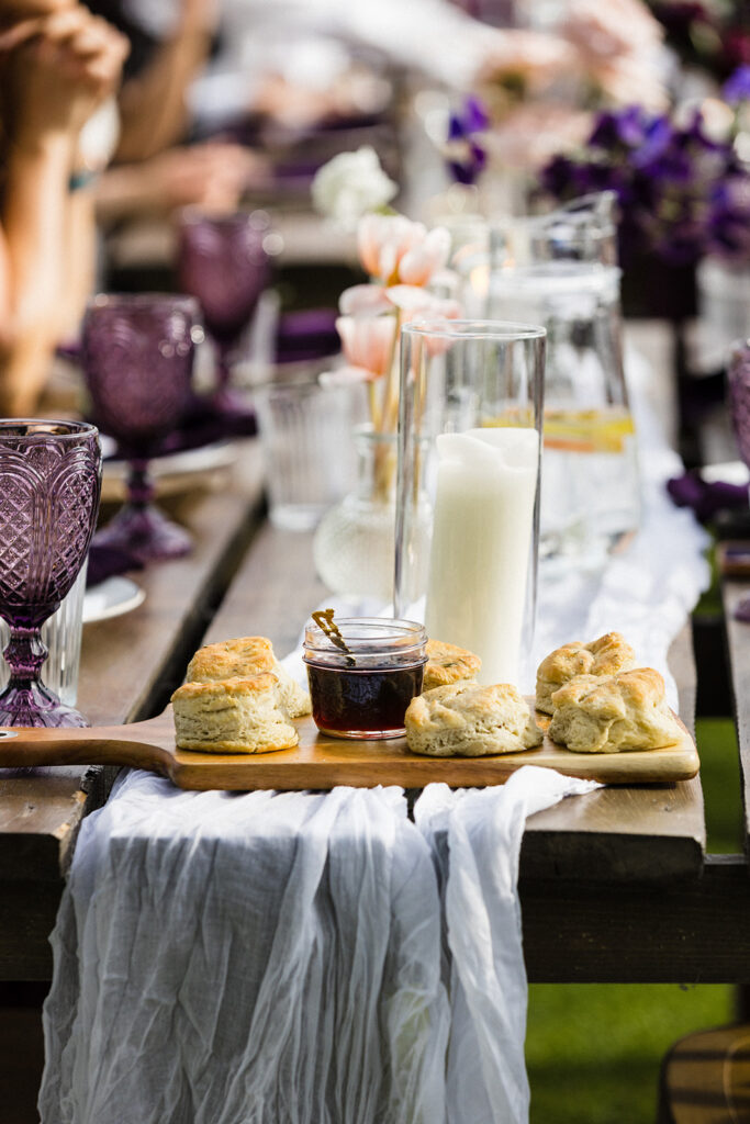 An elegantly set outdoor dining table with scones, jam, and candles, ready for a garden party.