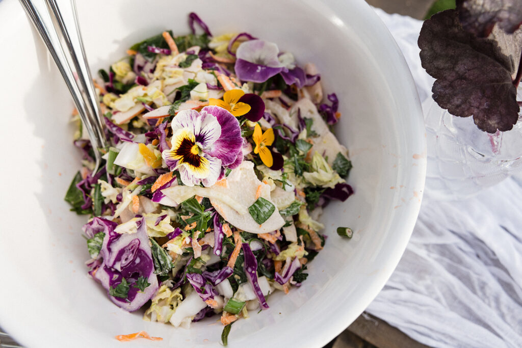 A fresh mixed salad garnished with edible flowers in a white bowl.