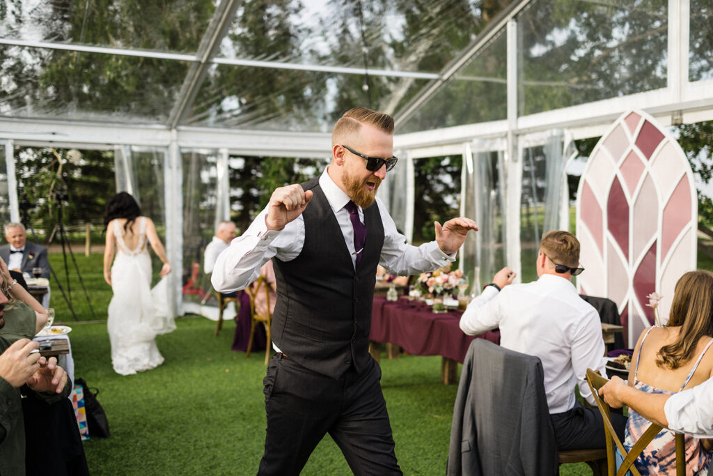 Man in sunglasses dancing at an outdoor wedding reception.