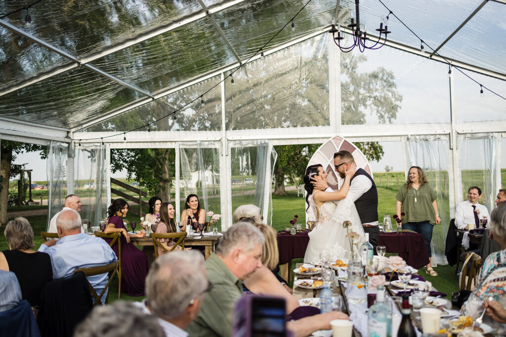 Bride and groom sharing a dance under a transparent tent at an outdoor wedding reception while guests look on.
