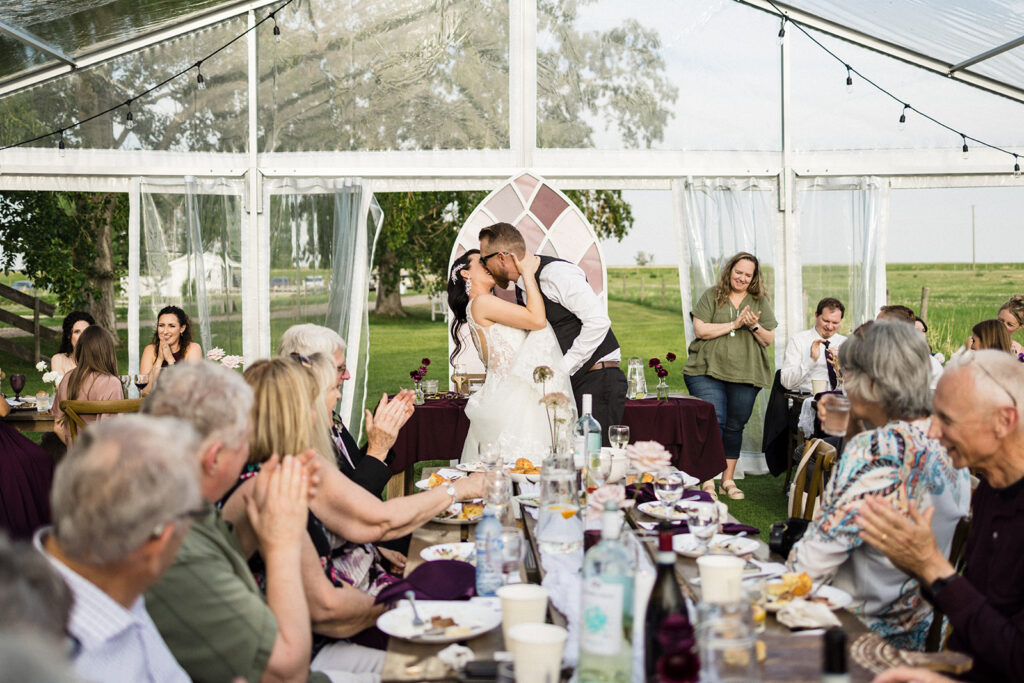 A couple kissing at their wedding reception while guests applaud.