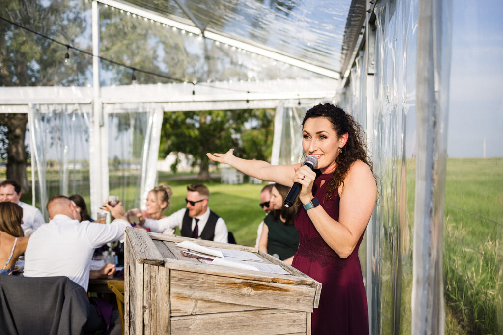 Woman giving a speech at an outdoor event with guests seated at tables.