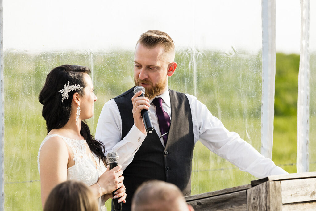 A bride and groom speaking into microphones at an outdoor wedding ceremony.