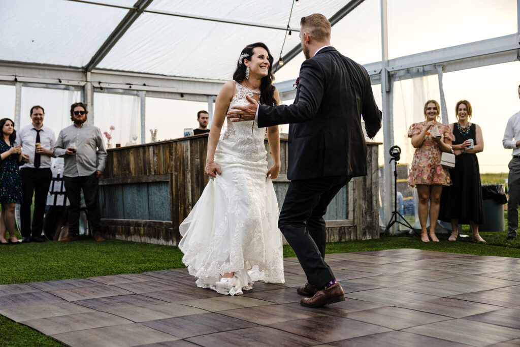 Bride and groom sharing a dance on an outdoor wooden floor with guests watching.