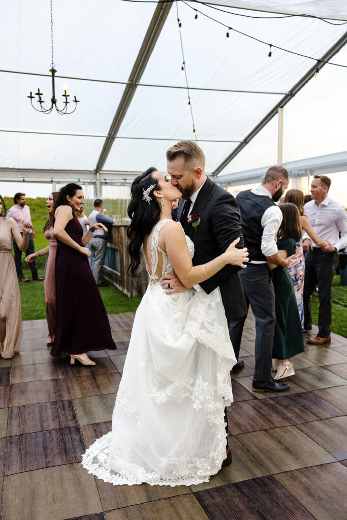 Bride and groom sharing a kiss on the dance floor under a tent at a wedding reception.