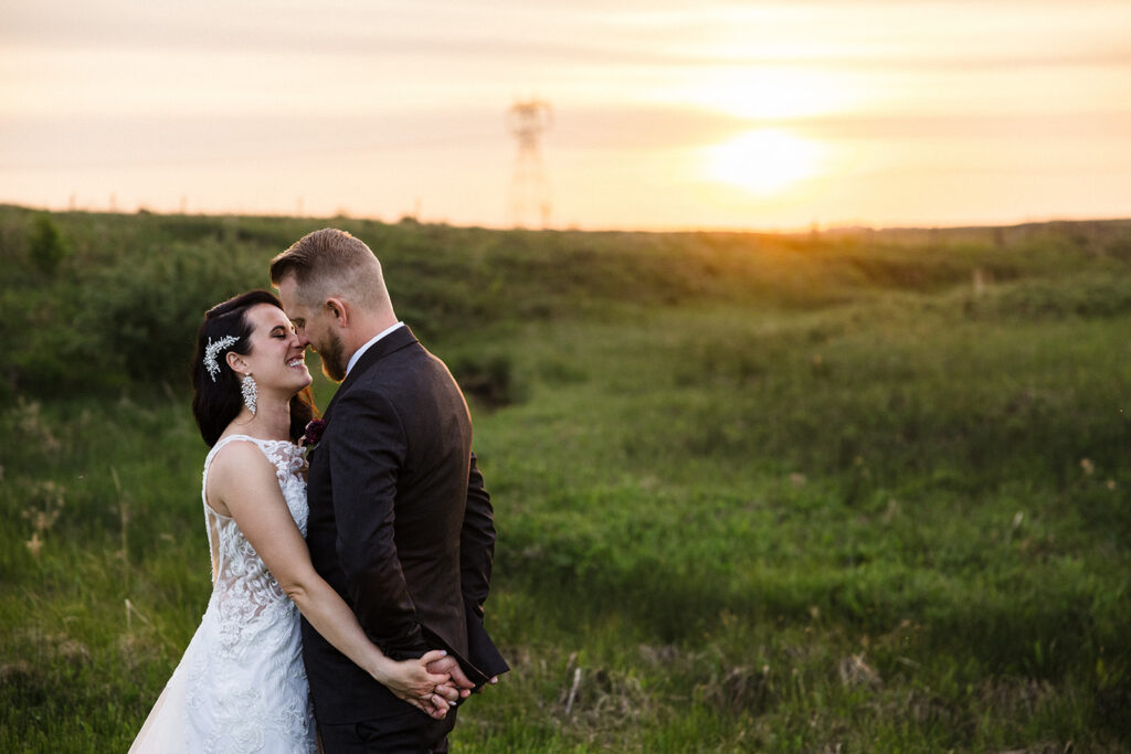 A bride and groom embracing in a field at sunset.