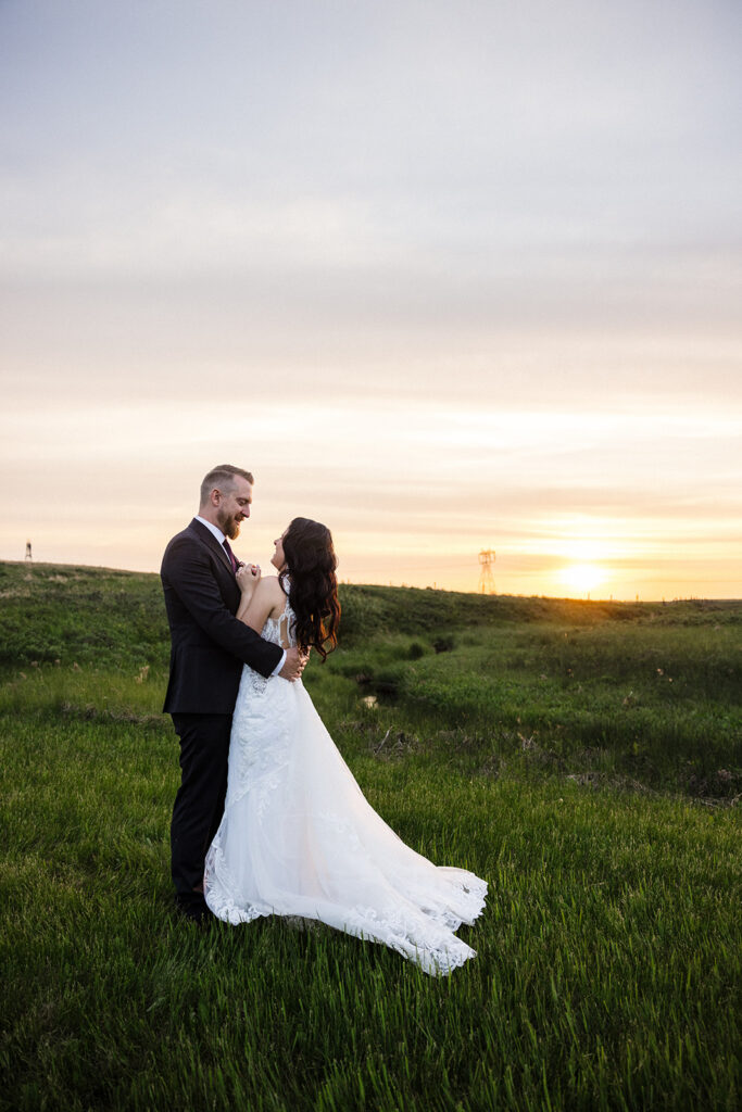 A couple embracing in a field at sunset on their wedding day.