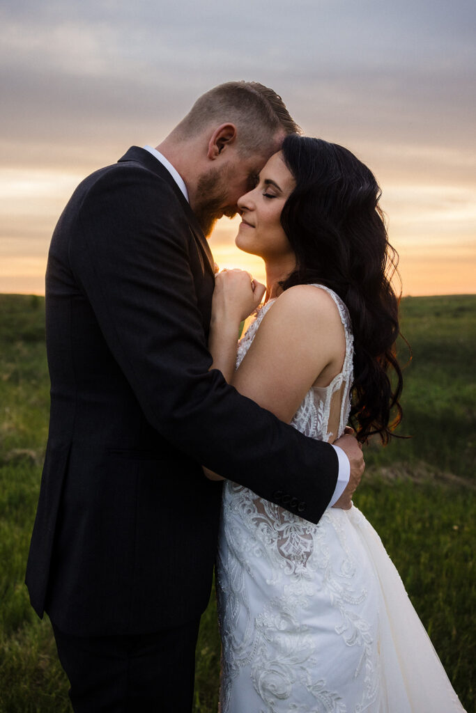 A couple in wedding attire sharing an intimate moment at sunset in a field.