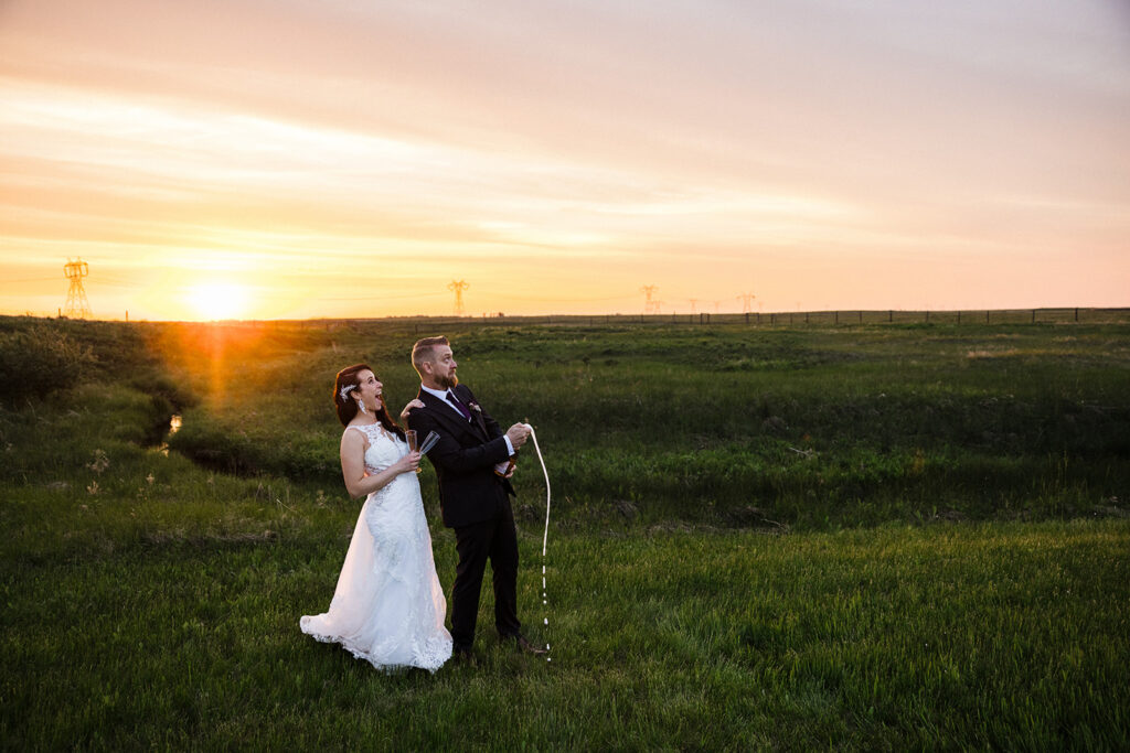 A bride and groom pose in a sunset-lit field.