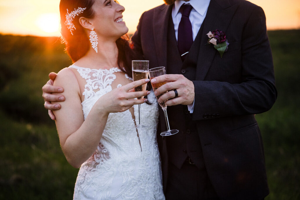 A bride and groom toasting with champagne glasses at sunset.