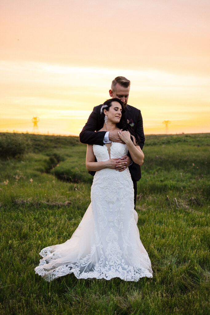 Bride and groom embracing in a field at sunset.