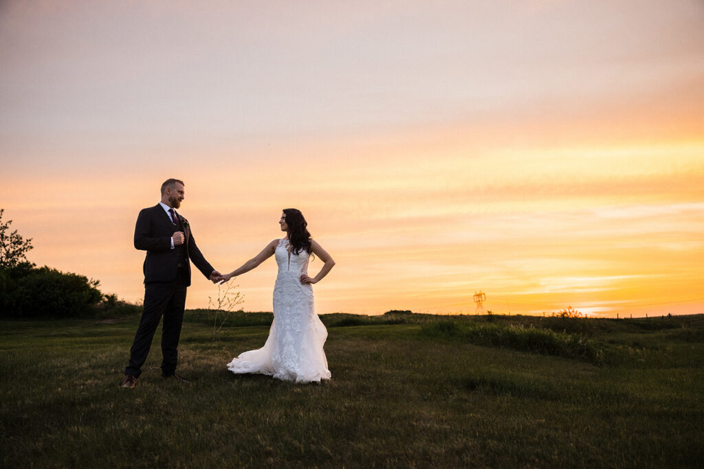Bride and groom holding hands in a field at sunset.