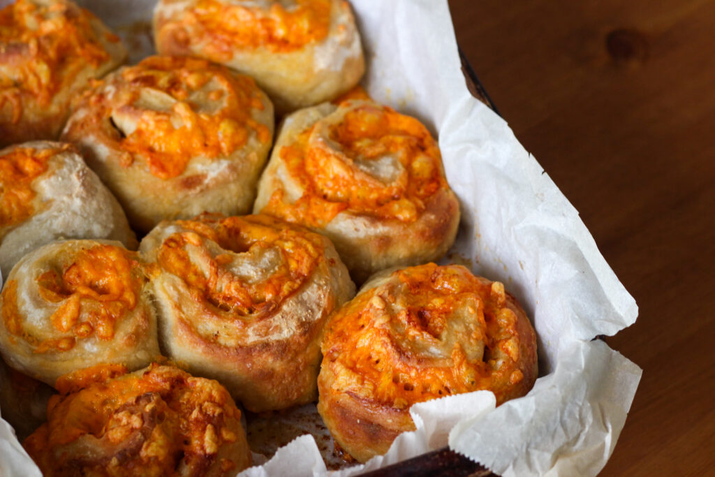 Freshly baked cheese-topped rolls in a baking dish.Irresistible Sourdough Cheese Buns