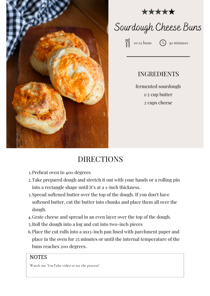 Freshly baked sourdough cheese buns on a wooden surface with a recipe card beside them.